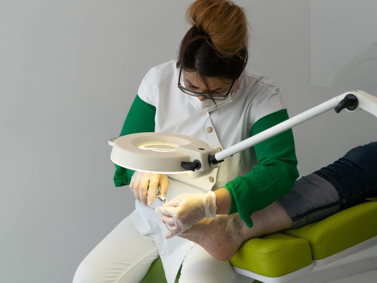 Podologin behandelt mit Handschuhen und Lupenlampe einen Fuß